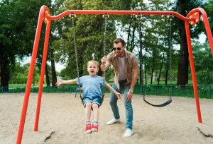 Man pushing child on swing - playgrounds are one of many services offered by local government