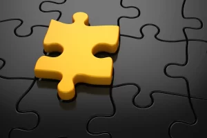 A 3D rendering of a yellow puzzle piece standing out from a mostly black puzzle, symbolizing a unique solution or missing piece.